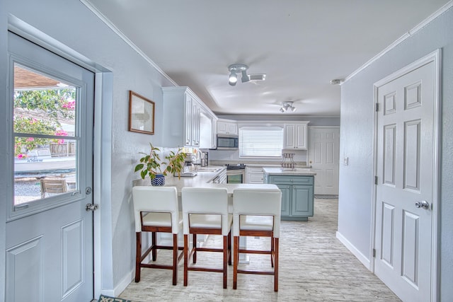 kitchen featuring light countertops, ornamental molding, a peninsula, white cabinets, and stainless steel appliances