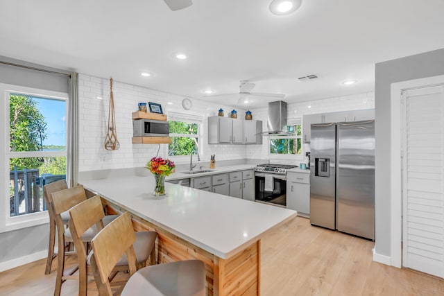 kitchen featuring appliances with stainless steel finishes, kitchen peninsula, extractor fan, and gray cabinetry