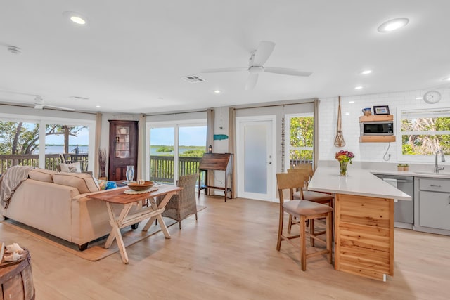 interior space with sink, light hardwood / wood-style flooring, a breakfast bar, built in microwave, and stainless steel dishwasher