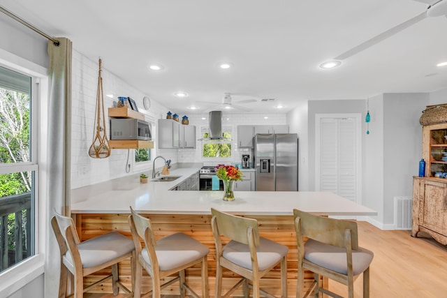 kitchen with island range hood, sink, decorative backsplash, kitchen peninsula, and stainless steel appliances