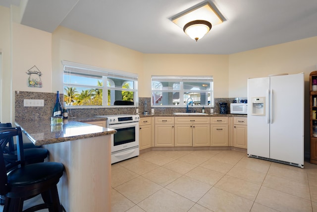 kitchen featuring sink, white appliances, decorative backsplash, kitchen peninsula, and dark stone counters