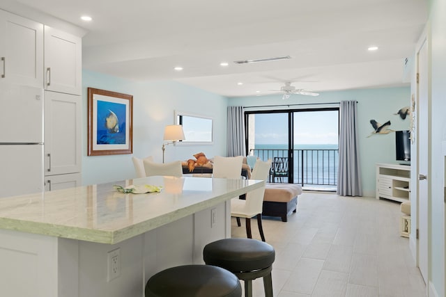 kitchen featuring a breakfast bar, white cabinetry, white refrigerator, ceiling fan, and light stone countertops