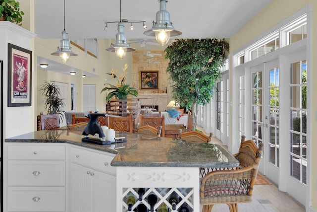 kitchen with open floor plan, white cabinetry, dark stone counters, french doors, and hanging light fixtures