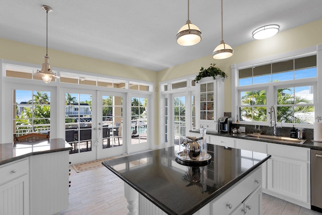 kitchen with dishwasher, white cabinets, pendant lighting, and a sink