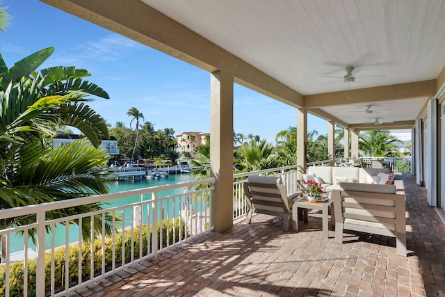 view of patio / terrace with an outdoor living space, a water view, a balcony, and a ceiling fan