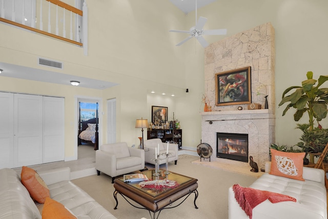 living area featuring visible vents, baseboards, ceiling fan, a fireplace, and a towering ceiling