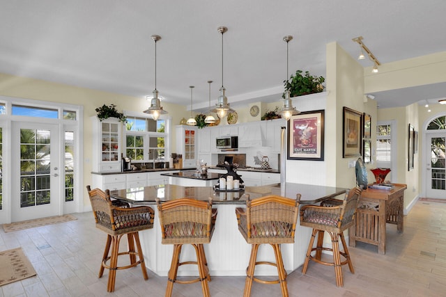 kitchen with a sink, stainless steel microwave, dark countertops, white cabinetry, and light wood finished floors