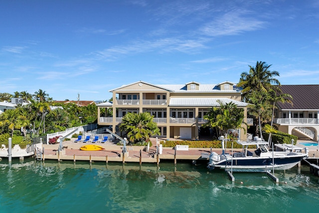 rear view of property with boat lift, metal roof, a water view, and a balcony