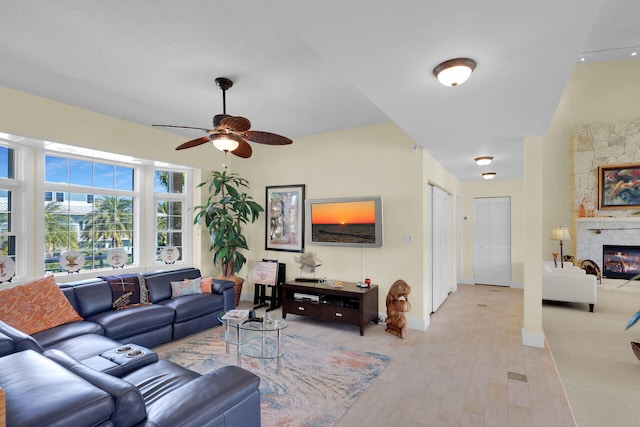 living room featuring a fireplace, baseboards, light wood-style floors, and a ceiling fan