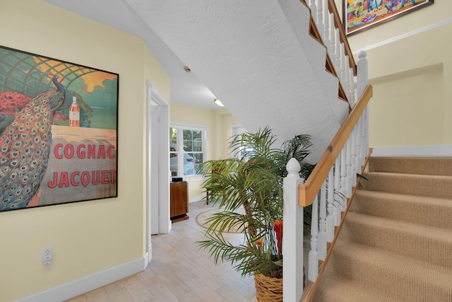 staircase featuring wood finished floors, baseboards, and a textured ceiling