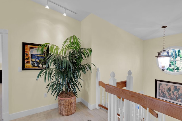 hallway featuring an upstairs landing, wood finished floors, an inviting chandelier, rail lighting, and baseboards