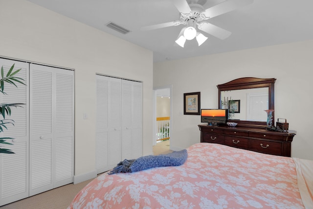 bedroom with visible vents, two closets, ceiling fan, and carpet flooring