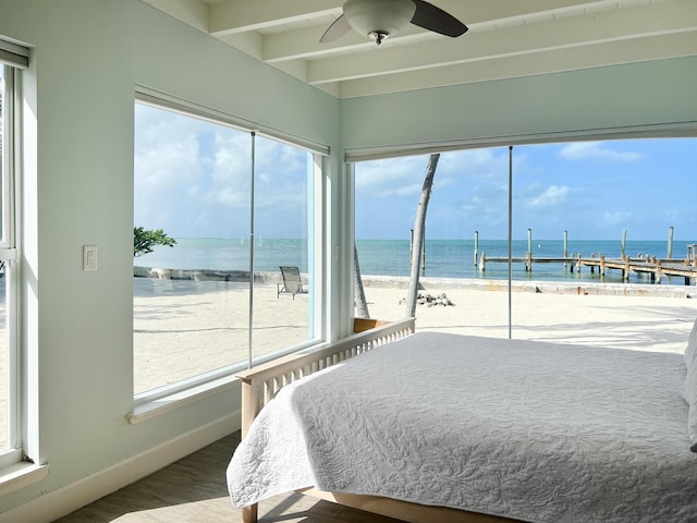 bedroom with hardwood / wood-style flooring, a water view, ceiling fan, and a view of the beach