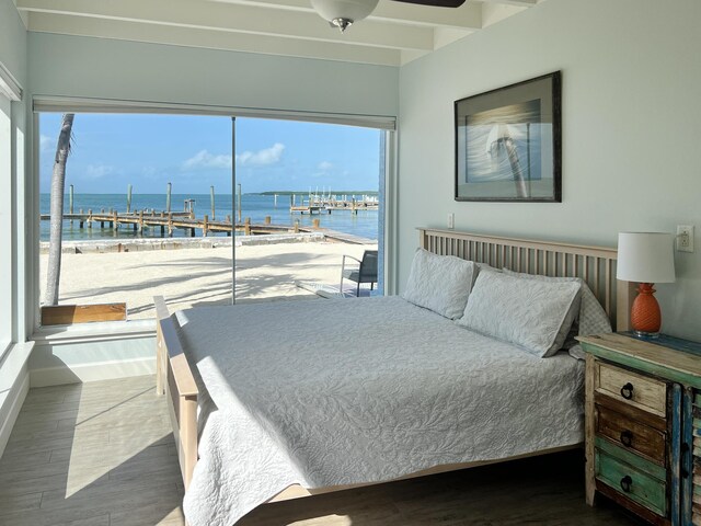 bedroom featuring a water view, access to outside, hardwood / wood-style floors, and a view of the beach