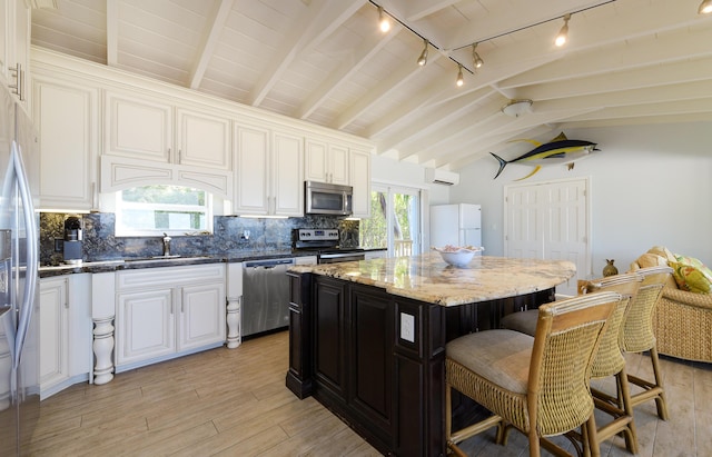 kitchen with sink, a center island, lofted ceiling with beams, dark stone countertops, and appliances with stainless steel finishes