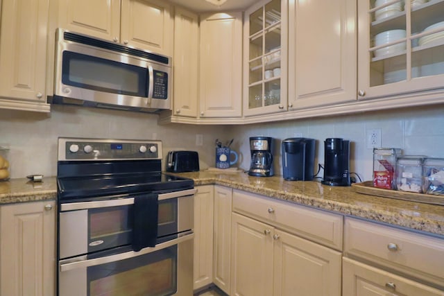 kitchen featuring glass insert cabinets, appliances with stainless steel finishes, light stone counters, and backsplash