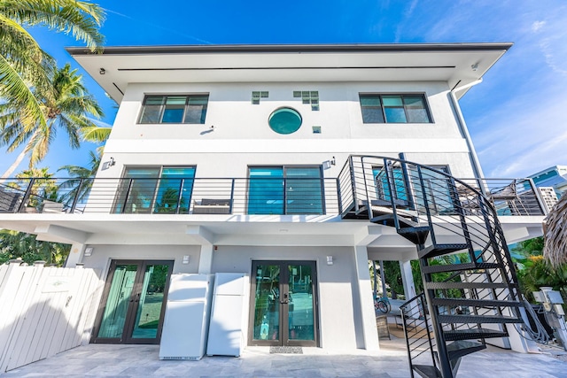 rear view of house with stucco siding, french doors, a balcony, and fence