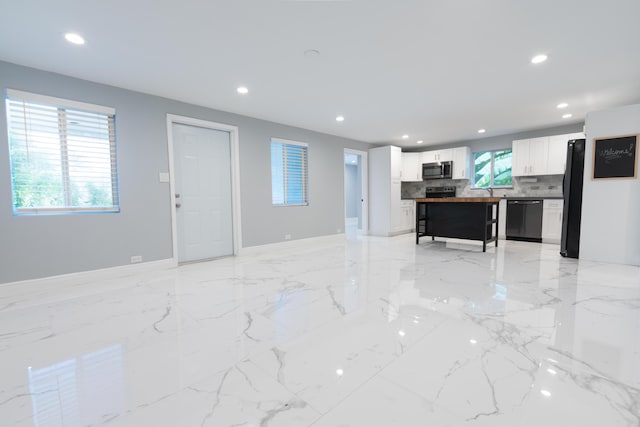 interior space featuring tasteful backsplash, black appliances, a center island, and white cabinets