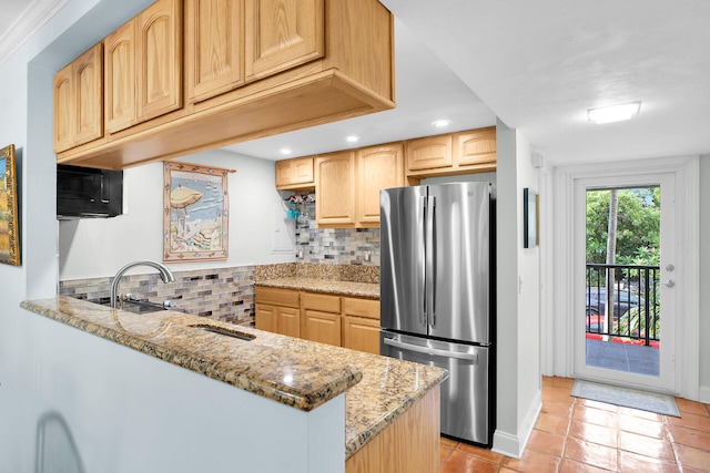 kitchen with stainless steel fridge, backsplash, light stone countertops, light brown cabinetry, and kitchen peninsula