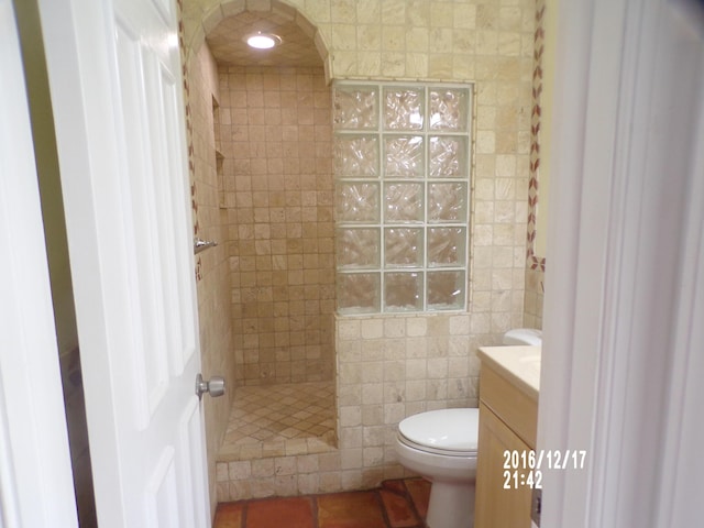 bathroom with tile walls, a tile shower, vanity, tile patterned floors, and toilet