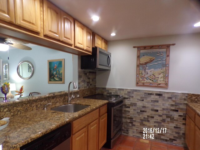 kitchen with sink, tile walls, dark tile patterned floors, light stone counters, and stainless steel appliances