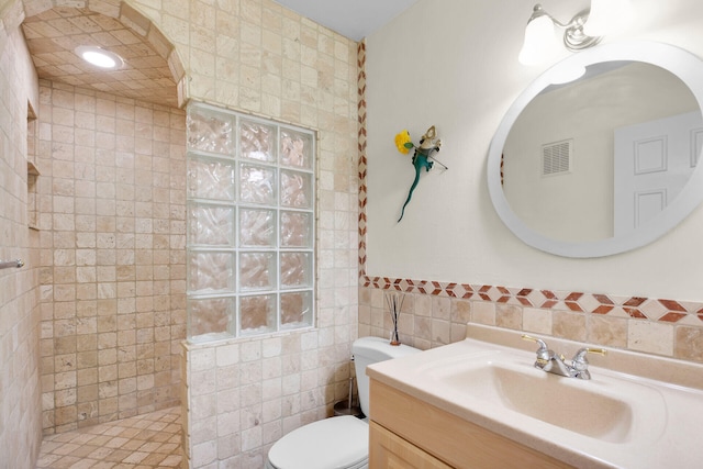 bathroom with vanity, a tile shower, tile walls, and toilet