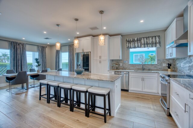 kitchen with white cabinetry, decorative light fixtures, stainless steel appliances, and a center island