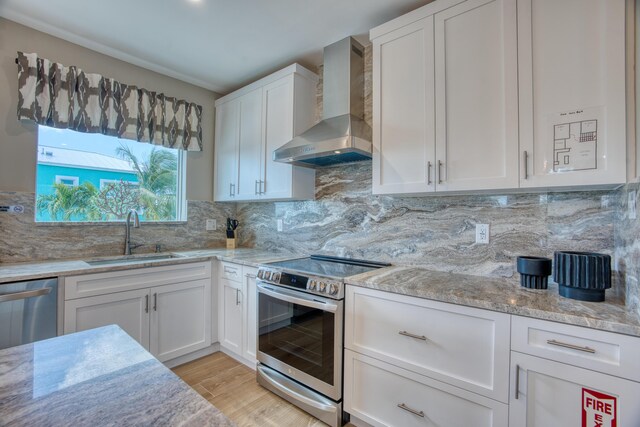 kitchen featuring white cabinetry, wall chimney range hood, sink, and appliances with stainless steel finishes