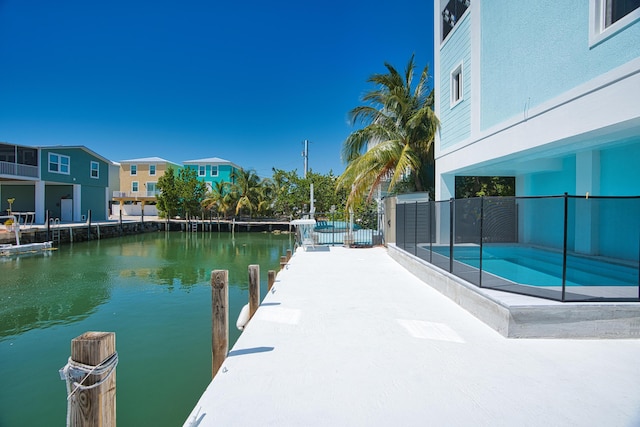 dock area featuring a water view, a fenced in pool, and a patio