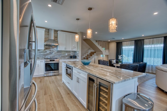 kitchen featuring pendant lighting, stainless steel appliances, white cabinets, a kitchen island, and wall chimney exhaust hood