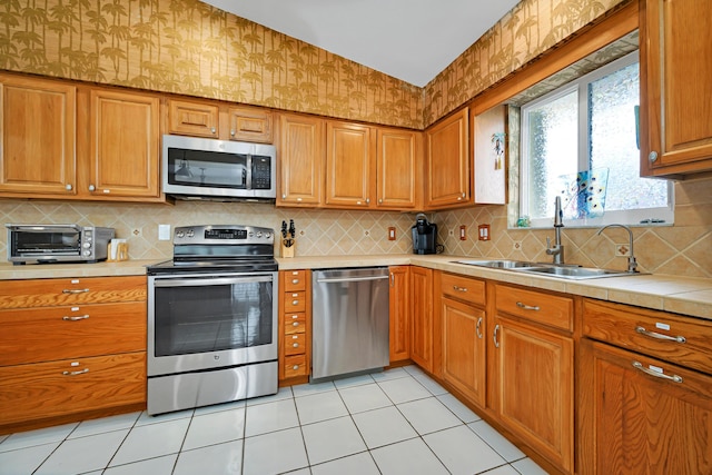 kitchen with sink, light tile patterned floors, stainless steel appliances, and decorative backsplash