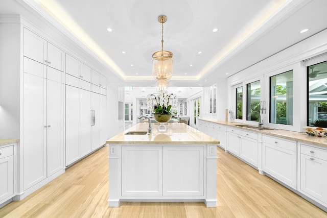 kitchen featuring pendant lighting, white cabinetry, sink, a raised ceiling, and a center island with sink