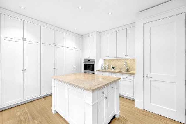 kitchen with sink, light hardwood / wood-style flooring, a center island, white cabinets, and oven