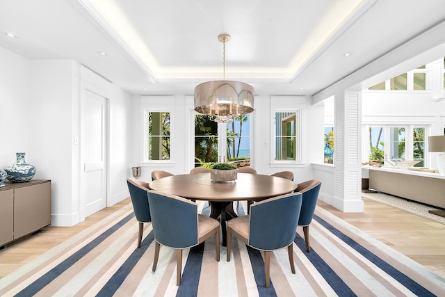 dining room with an inviting chandelier, a raised ceiling, and light wood-type flooring