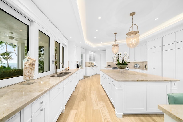 kitchen with white cabinetry, a tray ceiling, sink, and hanging light fixtures