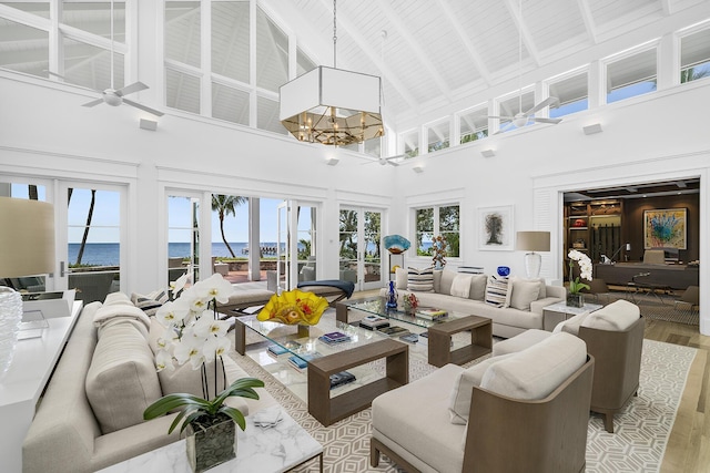 living room with light hardwood / wood-style flooring, beam ceiling, high vaulted ceiling, a water view, and ceiling fan with notable chandelier