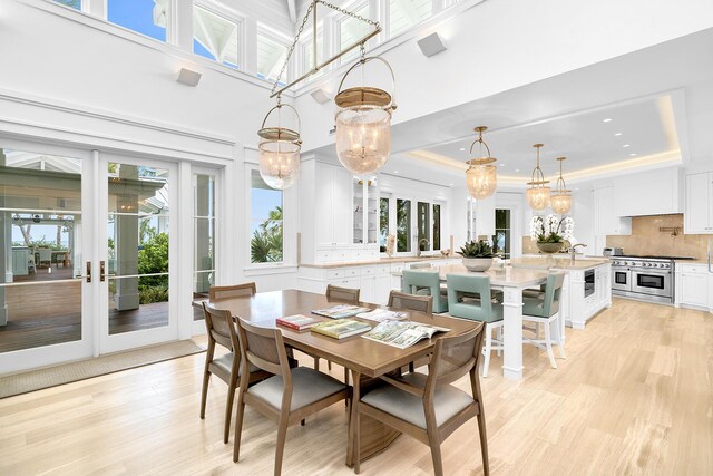 dining space featuring french doors, sink, a chandelier, light hardwood / wood-style flooring, and a raised ceiling