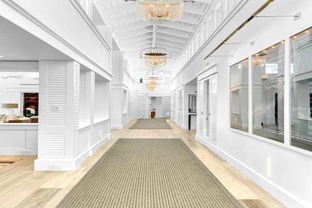 hall with beamed ceiling, high vaulted ceiling, light wood-type flooring, and an inviting chandelier