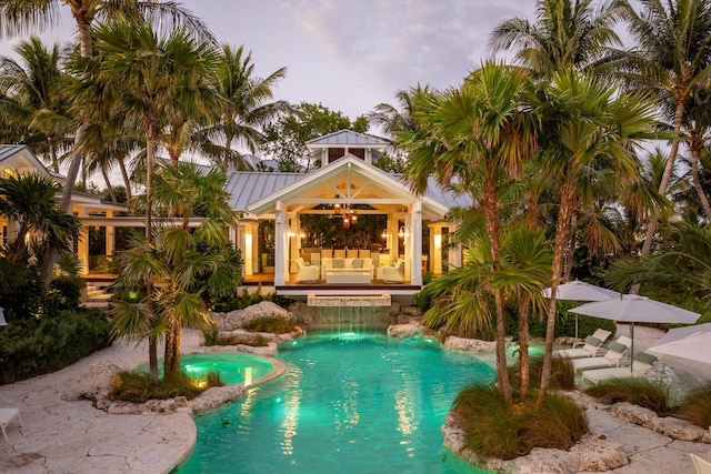 pool at dusk featuring an in ground hot tub, outdoor lounge area, ceiling fan, and a patio