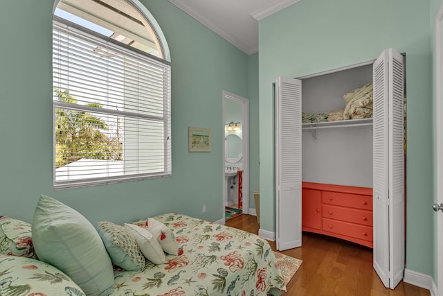 bedroom with wood finished floors, baseboards, ensuite bath, ornamental molding, and a closet