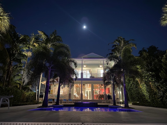 view of front facade featuring a balcony, a ceiling fan, and a pool with connected hot tub