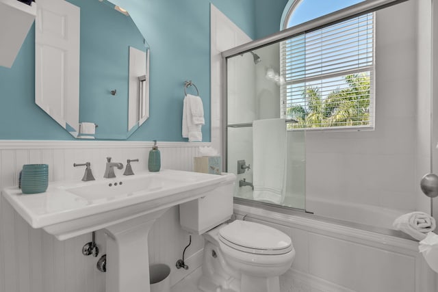 bathroom featuring toilet, bath / shower combo with glass door, and wainscoting