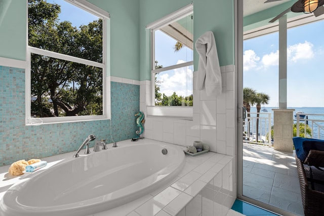 full bathroom with ceiling fan, tile walls, tiled tub, and a water view