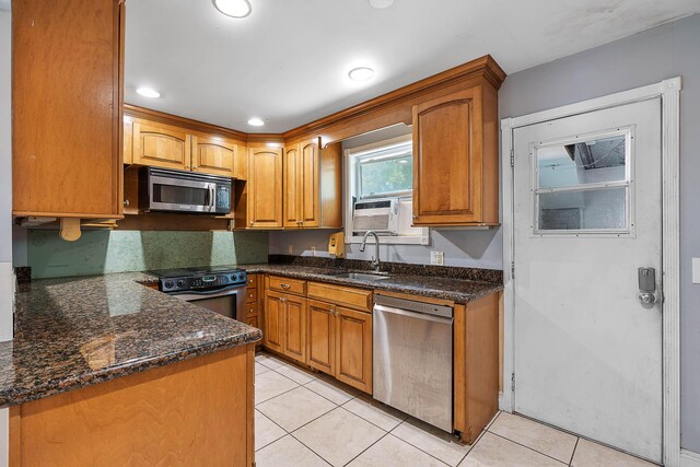 kitchen featuring dark stone counters, light tile patterned flooring, appliances with stainless steel finishes, and a sink