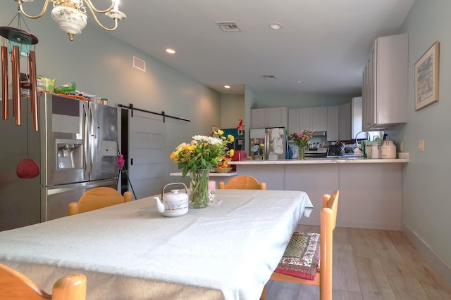 dining space with a barn door, light wood-type flooring, recessed lighting, a chandelier, and baseboards