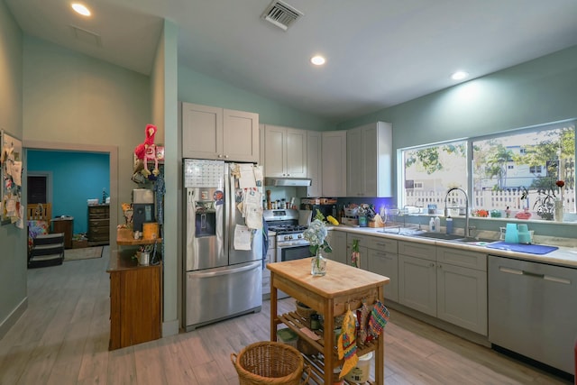 kitchen featuring stainless steel appliances, a sink, lofted ceiling, light wood-type flooring, and light countertops