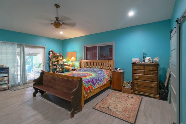 bedroom featuring a barn door, wood finished floors, a ceiling fan, recessed lighting, and access to exterior