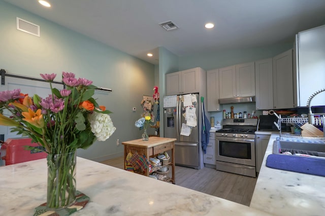 kitchen featuring stainless steel appliances, under cabinet range hood, a sink, light wood finished floors, and recessed lighting