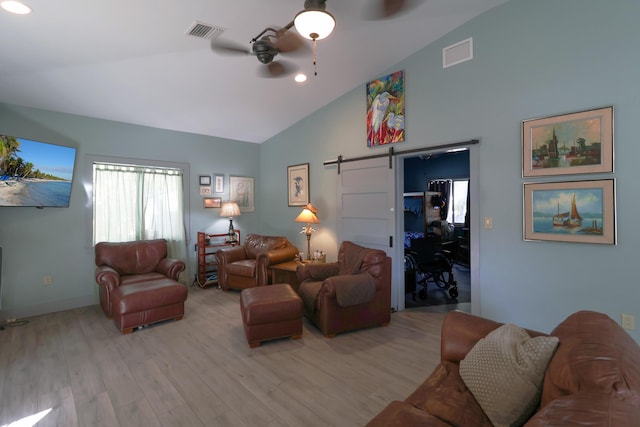 living room with a barn door, a ceiling fan, light wood finished floors, and high vaulted ceiling