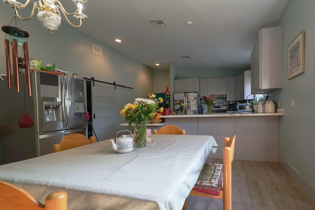 dining space with a barn door, light wood-type flooring, recessed lighting, baseboards, and lofted ceiling